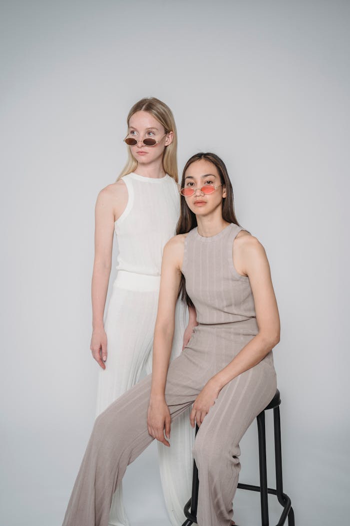 Two stylish women posing with sunglasses in a studio setting.